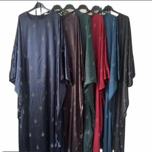 May include: A selection of long, flowing dresses in shades of navy, brown, green, red, teal, and black. Each dress has long sleeves and a repeating leaf pattern. They are displayed on black hangers.