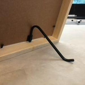 May include: A black metal easel stand for a picture frame. The stand is attached to the back of the frame and folds out to prop the frame up.