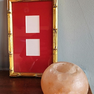 Op de afbeelding: Een gouden fotolijst met twee lege witte passe-partouts op een rode achtergrond. Een roze Himalaya-zoutlamp staat op een houten oppervlak.
