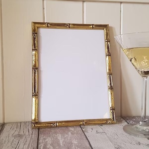 May include: A gold-colored picture frame with a bamboo-style design. The frame is empty and has a white background.