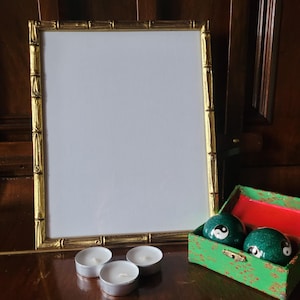 Könnte beinhalten: Ein goldener Bambusrahmen mit einem weißen Passepartout und einem weißen Hintergrund. Drei weiße Teelichter befinden sich im Vordergrund. Eine grüne Box mit rotem Innenraum und zwei schwarz-weiße Yin-Yang-Kugeln befindet sich in der unteren rechten Ecke.