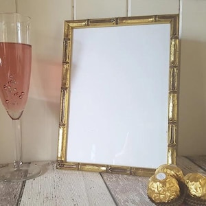 May include: A gold picture frame with a bamboo design. The frame is empty and has a white mount. There are three chocolate sweets in the foreground.