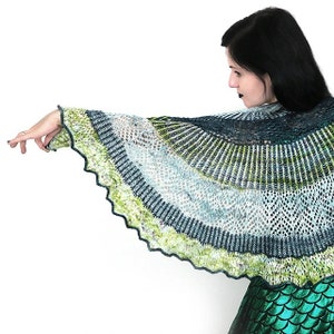 May include: A green, blue and white crocheted shawl with a scalloped edge. The shawl is draped over the shoulders of a person wearing a green sequined skirt.