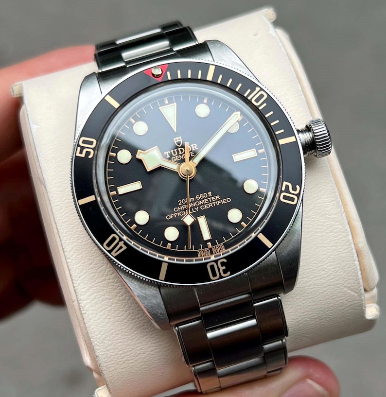 May include: A stainless steel wristwatch with a black dial and a black rotating bezel. The watch features luminous hands and markers, a date display, and a metal band. The watch is displayed on a white surface.