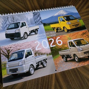 Peut inclure: Calendrier mensuel 2026 de camions Kei japonais, relié en spirale. Il présente quatre images de camions dans différents environnements. Le texte "Japanese Kei Truck Monthly Calendar" et l'année "2026" sont visibles. Les camions sont blancs, jaunes et argentés.
