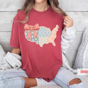 a woman sitting on a bed wearing a red shirt with a map of the united