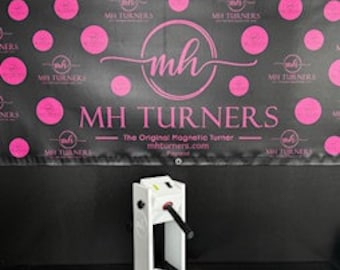 May include: A white and black heat press machine with a lever handle. The machine is in front of a black banner with pink polka dots and the text "MH TURNERS - The Original Magnetic Turner - mhturners.com".