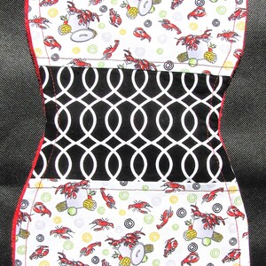 May include: A padded bib with a red trim. The top and bottom sections feature a white background with a pattern of red crawfish, corn, and lemons. The center section has a black and white geometric design.