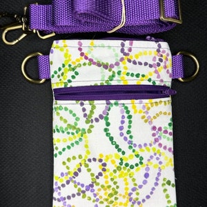 May include: A white fabric pouch with a purple zipper and a purple strap. The pouch has a colorful pattern of green, yellow, and purple circles.