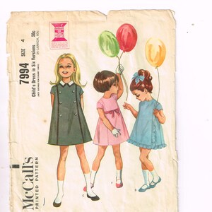 Puede incluir: Patrón impreso vintage de McCall's para un vestido de niña en seis versiones, talla 4. La ilustración muestra a tres niñas pequeñas con diferentes vestidos y globos. El patrón incluye el texto "Child's Dress in Six Versions".