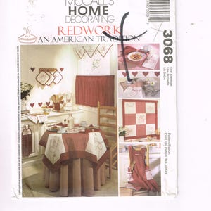 May include: McCall's Home Decorating Redwork pattern. The image shows a kitchen scene with red and white textiles, including a table skirt, curtains, and an apron. The design features heart and cherry motifs.