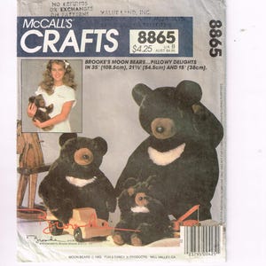 May include: McCall's Crafts pattern featuring Brooke's Moon Bears. The pattern includes instructions for making three plush bears: 35 inches (88.9 cm), 21.5 inches (54.6 cm), and 15 inches (38.1 cm) tall. The image shows the bears and a woman holding one.