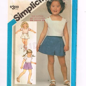Puede incluir: Patrón de costura Simplicity para un conjunto infantil, con top blanco y shorts azules. El patrón incluye ilustraciones del conjunto y el texto "Simplicity" y "Talla 4 Niño". El precio es de $3.00 U.S.A.