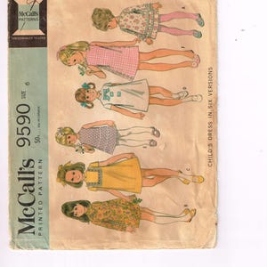 Puede incluir: Sobre de patrón McCall's vintage, con ilustraciones de seis vestidos infantiles diferentes. El sobre es de color beige con el logotipo de McCall's y el número de patrón 9590. Los vestidos son de varios colores y estampados, incluyendo floral y cuadros.