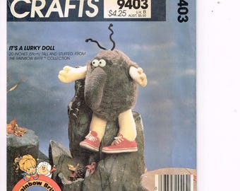 Puede incluir: Patrón de McCall's Crafts para una muñeca Lurky, de 51 cm de altura, de la colección Rainbow Brite. La muñeca es gris con brazos y piernas amarillas, con zapatillas rojas. La portada del patrón es azul.