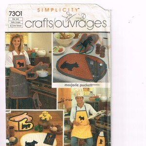 May include: Simplicity crafts/ouvrages pattern 7301. The image shows a pattern for kitchen accessories, including aprons, oven mitts, and placemats. The pattern features a black dog silhouette design. The text "26 wide" is visible.