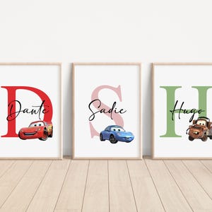 Puede incluir: Tres impresiones enmarcadas con una letra grande, un nombre y un coche de dibujos animados. La primera impresión es roja con la letra D y el nombre Dante, la segunda impresión es rosa con la letra S y el nombre Sadie, y la tercera impresión es verde con la letra H y el nombre Hugo.