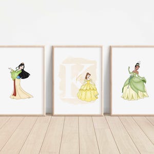 Può includere: Tre stampe incorniciate con principesse Disney. La stampa a sinistra mostra Mulan nel suo vestito verde e giallo. La stampa al centro mostra Belle nel suo vestito giallo con la lettera "B" sullo sfondo. La stampa a destra mostra Tiana nel suo vestito verde e giallo.