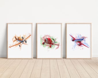 May include: Three framed watercolor prints of airplanes. The planes are in shades of orange, red, and blue, with brown frames. Each plane has a unique design and is set against a colorful watercolor splash background. The prints are displayed on a light wood floor.