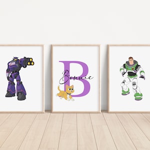 May include: Three framed prints with cartoon characters. The left print features a purple robot with yellow accents. The middle print features a purple letter B with the name Bonnie written in cursive. The right print features a cartoon character in a space ranger costume.