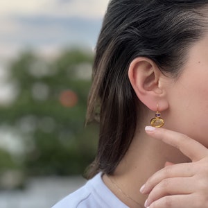 May include: Gold earrings with a yellow oval gemstone and a small purple square gemstone.