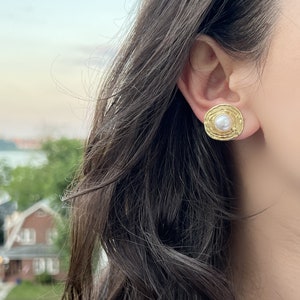 May include: Gold tone earrings with a textured circular design and a white pearl in the center.