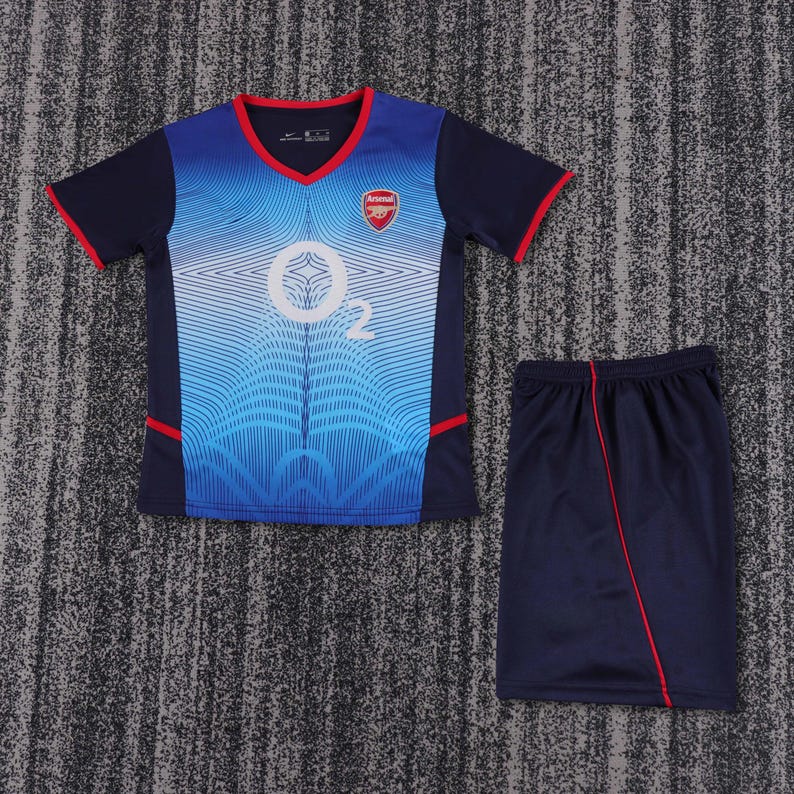 May include: A blue and white football shirt with a red and white team logo and the word "Arsenal" on the front. The shirt is paired with navy blue shorts with a red stripe down the side.