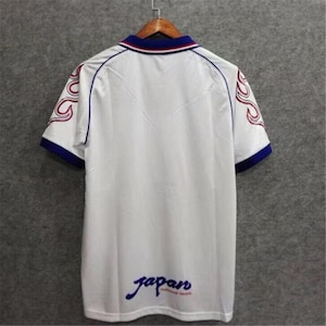 May include: White football shirt with blue and red trim. The shirt has a flame design on the sleeves and the word "Japan" written on the back.