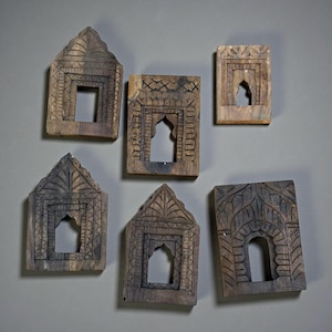 May include: Six intricately carved wooden window frames with varying geometric and arched designs. The frames are a warm brown colour, with dark detailing, and are arranged against a neutral grey background. Each frame features a central opening, showcasing the detailed craftsmanship.