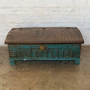 May include: A weathered wooden trunk with a curved top. The top is a dark brown color, while the body is a distressed teal. A brass-colored lock is centered on the front. The trunk is a decorative storage piece.