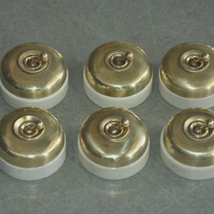 May include: Six vintage-style light switches. Each switch features a brass-colored, domed cover with a central toggle and a white ceramic base. The switches are arranged in two rows of three.