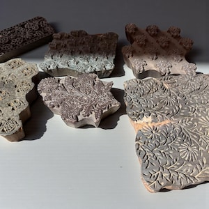 Könnte beinhalten: Eine Sammlung geschnitzter Holz-Druckblöcke mit floralen und geometrischen Mustern. Die Blöcke variieren in Größe und Form, mit Farben von hellbraun bis dunkelgrau. Die filigranen Designs sind auf den Oberflächen der Blöcke sichtbar.
