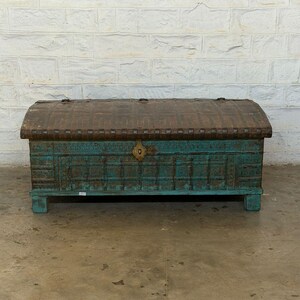 May include: A weathered, antique wooden chest with a turquoise base and a curved, brown metal top. The chest features intricate carved details and a brass lock. The trunk is a decorative storage piece.