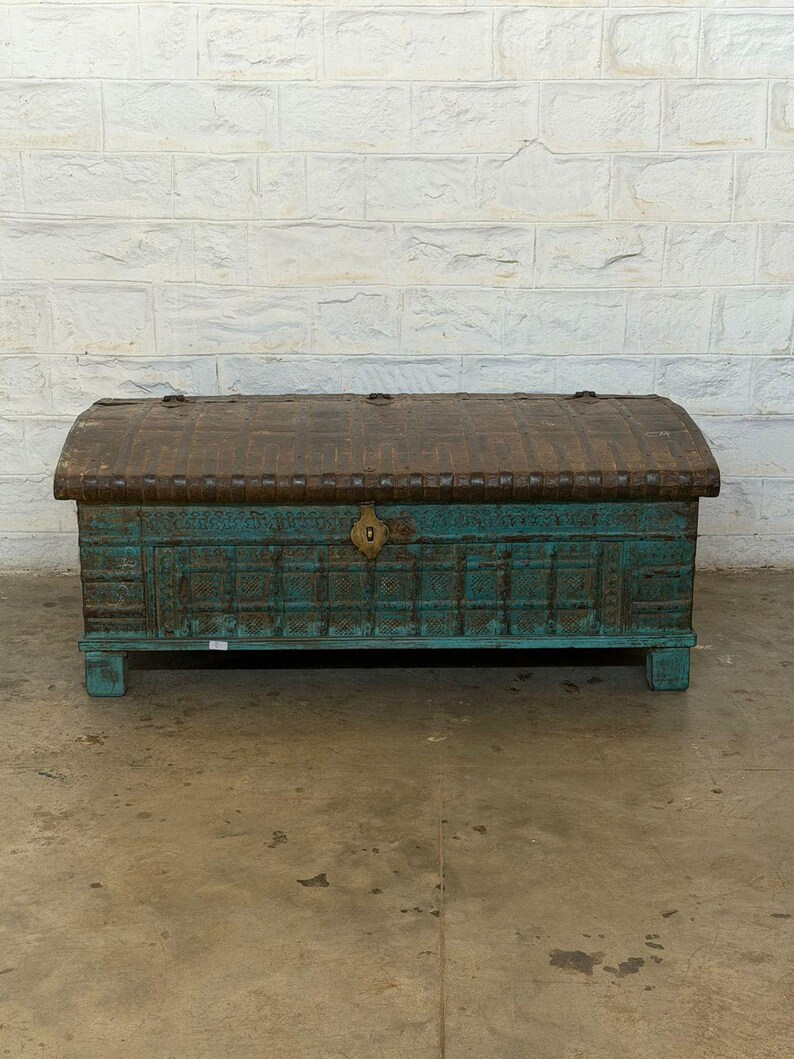May include: A weathered, antique wooden chest with a turquoise base and a curved, brown metal top. The chest features intricate carved details and a brass lock. The trunk is a decorative storage piece.