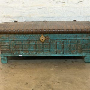 May include: A large, antique wooden chest with a turquoise finish and a brown, arched lid. The chest features intricate carvings and a brass lock. It sits on short, square legs, and is a decorative storage piece.
