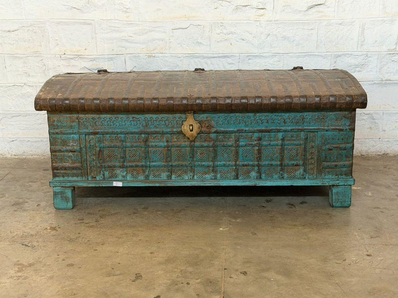 May include: A large, antique wooden chest with a turquoise finish and a brown, arched lid. The chest features intricate carvings and a brass lock. It sits on short, square legs, and is a decorative storage piece.