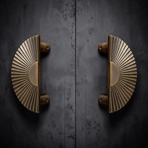 May include: Two semi-circular door handles made of brushed brass with a radiating sunburst pattern. Each handle features a flat vertical edge and a curved outer rim with deep grooves, mounted with two cylindrical attachment points on each side.