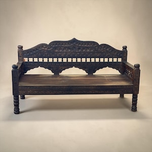 May include: A dark brown wooden bench featuring intricate hand-carved floral and geometric patterns across the backrest, armrests, and legs. The bench has a flat seat, a high arched back with spindle details, and four sturdy, carved cylindrical legs.