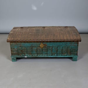 May include: A rectangular antique trunk with a teal body and a curved, brown metal lid. The trunk features decorative carvings and a brass latch. The wooden base is also teal. This vintage chest is a storage solution.