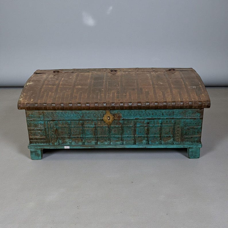 May include: A rectangular antique trunk with a teal body and a curved, brown metal lid. The trunk features decorative carvings and a brass latch. The wooden base is also teal. This vintage chest is a storage solution.