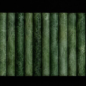 Puede incluir: Una colección de catorce varillas cilíndricas dispuestas en fila, cada una con un color verde bosque profundo con intrincados patrones de vetas de color verde más claro en toda la superficie, creando un aspecto marmolado uniforme en todas.