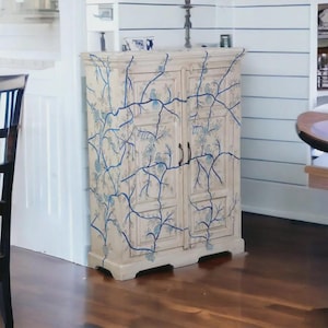 Peut inclure: Un buffet crème à deux portes, orné d'un motif de vigne florale bleue. Le buffet a des poignées marron foncé et repose sur une base basse. Le motif floral recouvre toute la surface du buffet.