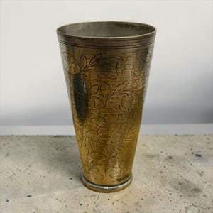 Puede incluir: Una taza de cerámica blanca con un asa negra y el texto "But First, Coffee" en negro y negrita. La taza está sobre una superficie blanca.