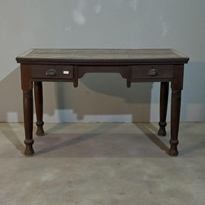 Könnte beinhalten: Ein dunkelbrauner Holzschreibtisch mit zwei Schubladen und Metallgriffen. Der Schreibtisch hat eine rechteckige Oberseite und vier gedrehte Beine. Der Schreibtisch ist ein Vintage-Stück, wahrscheinlich aus dem frühen 20. Jahrhundert. Der Schreibtisch ist in gutem Zustand und ca. 120 cm lang.