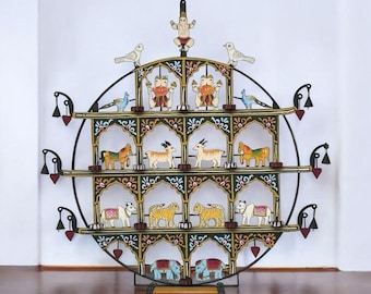 Puede incluir: Un adorno de pared circular de varios niveles con figuras de madera pintadas de animales, pájaros y deidades. El marco de metal negro tiene adornos florales y en forma de corazón. Las figuras están pintadas con colores vibrantes.