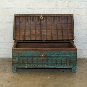 May include: An open, antique wooden chest with a teal base and a brown lid. The chest has intricate carvings and a brass clasp. The lid is propped open, revealing the empty interior. The chest is on short legs.