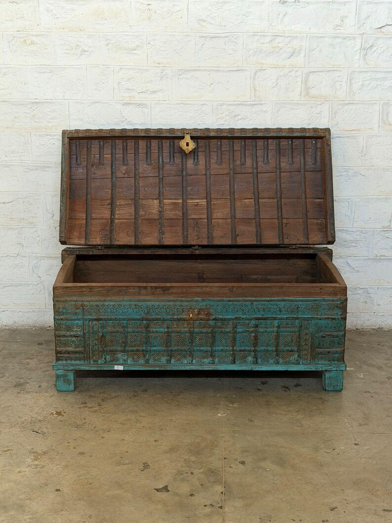 May include: An open, antique wooden chest with a teal base and a brown lid. The chest has intricate carvings and a brass clasp. The lid is propped open, revealing the empty interior. The chest is on short legs.