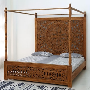 Può includere: Un letto a baldacchino in legno con intricati intagli floreali sulla testiera e sulla pediera. La struttura del letto è di colore marrone caldo e il letto è realizzato con un piumino fantasia e due cuscini.