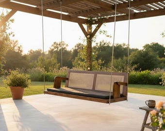 May include: A wooden swing bench with a woven back and a dark cushion hangs from a wooden pergola. The scene is set outdoors with potted plants and a natural backdrop, bathed in warm sunlight.