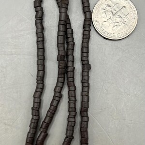 May include: Dark brown wooden bead strands with a dime for size comparison. The beads are cylindrical and strung together, creating a necklace or bracelet component. The beads are a deep, earthy tone.